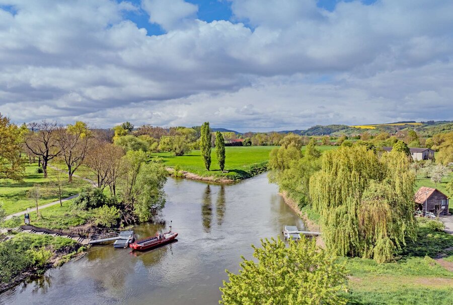 zwei Flussarme treffen sich, am Ufer liegen ein paar Schiffe, blauer Himmel mit Sonnenschein und frühlingshafter Natur