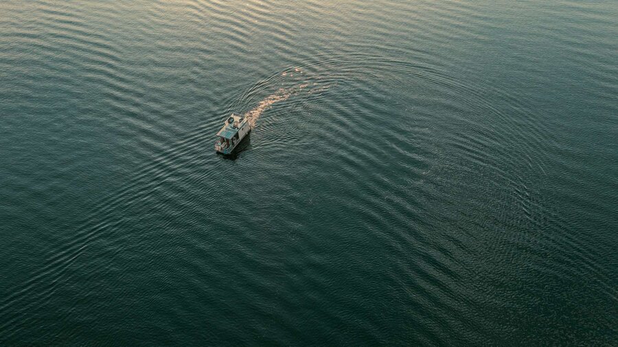 Hausboot fährt einsam auf dem Geiseltalsee, dessen Wasseroberfläche in der untergehenden Sonne glitzert